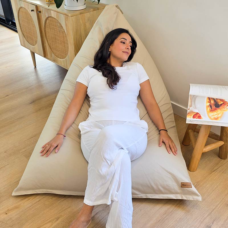 Natural oversized Cotton Canvas Triangle Indoor Bean Bag Chair by Mooi Living in a modern living room with soft neutral décor, woman seated.