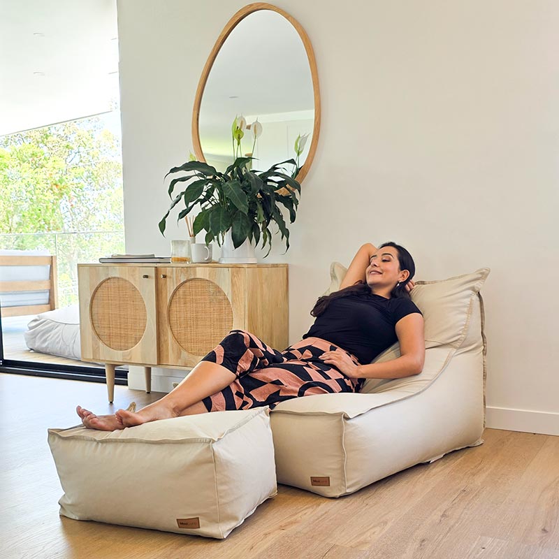 Natural cotton canvas Single Boss lounge chair positioned with coordinating ottoman in a refined home. Lady relaxes back into bean bag, with feet up on the ottoman.