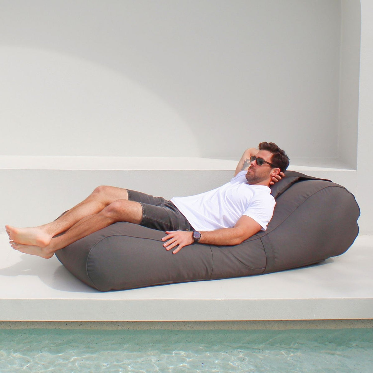 Man stretching out on a Mooi Living Oyster Black Isla outdoor bean bag sunlounger, showing its curved shape and raised backrest, MOISLABB- OYSB