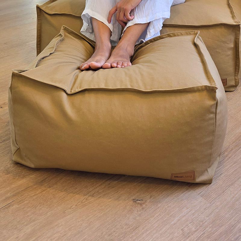 Tan canvas ottoman by Mooi Living positioned against a neutral wall.
