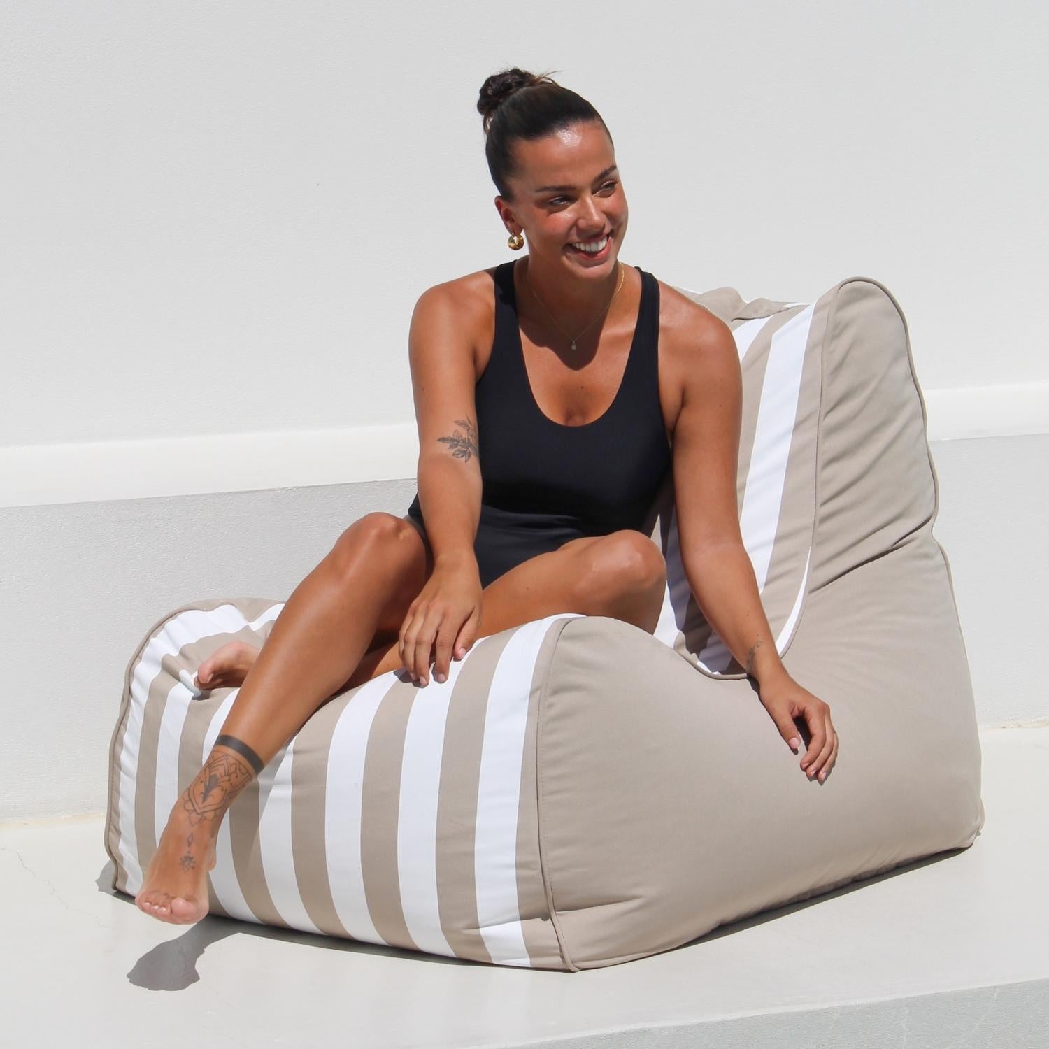 A woman sitting on a large beige and white striped outdoor bean bag chair against a clean white wall,MOBORABB-STRI-TAU