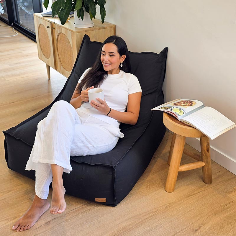 Woman seated on the Black Single Boss lounge-style bean bag by Mooi Living in a sleek interior setting.