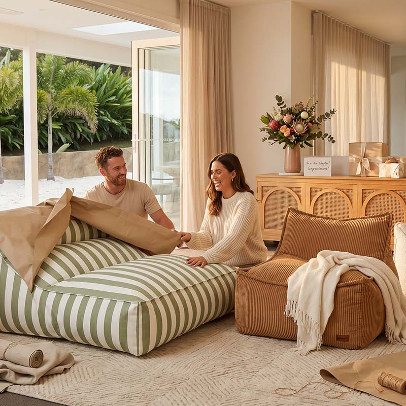 Man and woman sitting on Sage Green Lana Lounger outdoor bean bag by Mooi Living styled in a modern living room beside Mooi Living's Cord Chair in Caramel with a wooden sideboard and decorative pillows.