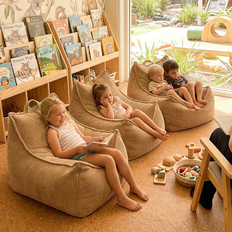 Lifestyle image of 3 Mini Cord Chairs indoor bean bag by Mooi Living in Caramel with children sitting on each bean bag in a room with bookshelves and toys while listening to their teacher reading a book.