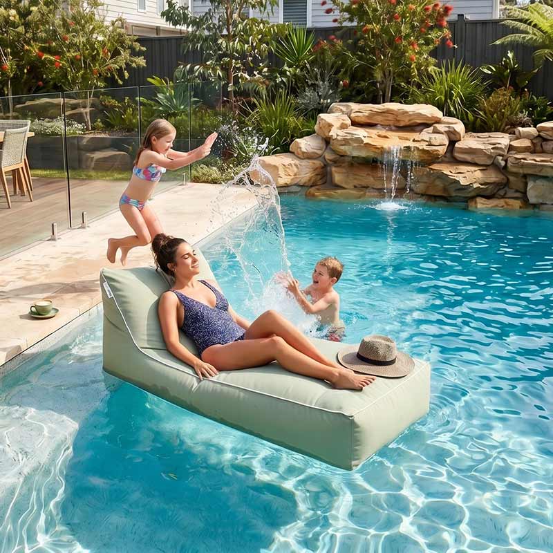 Woman relaxing on a Talia Float outdoor bean bag by Mooi Living in a pool with children playing nearby.