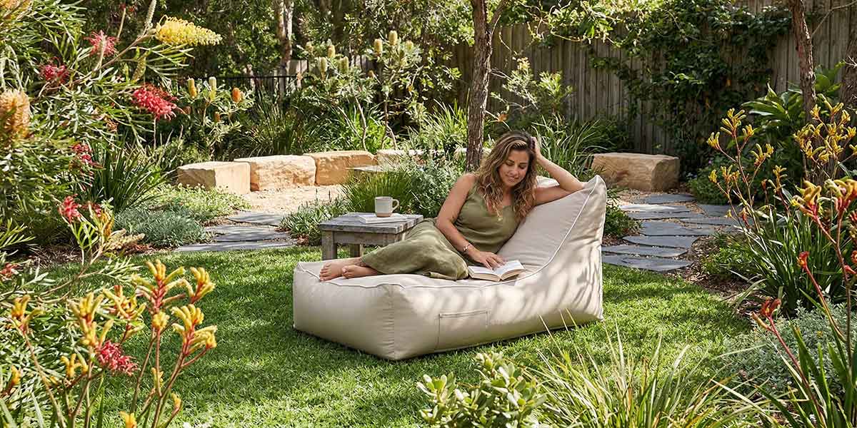 Lush Australian backyard garden with green lawn, native plants and soft landscaping, Lachlan Lounger outdoor bean bag by Mooi Living placed on the grass in dappled sunlight, calm outdoor retreat atmosphere.