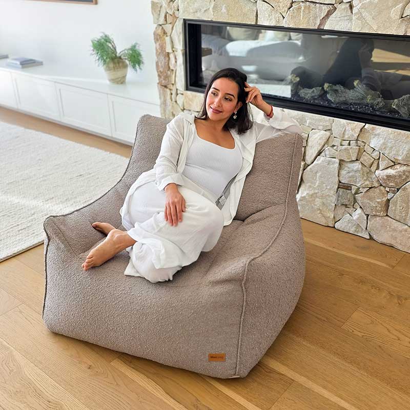 Woman seated on the Taupe Serena bouclé indoor bean bag chair in a contemporary home interior.