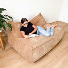 Mooi Living Double Seater Corduroy Bean Bag Lounger indoor bean bag by Mooi Living in Caramel in a neutral living room, woman relaxing with a book.