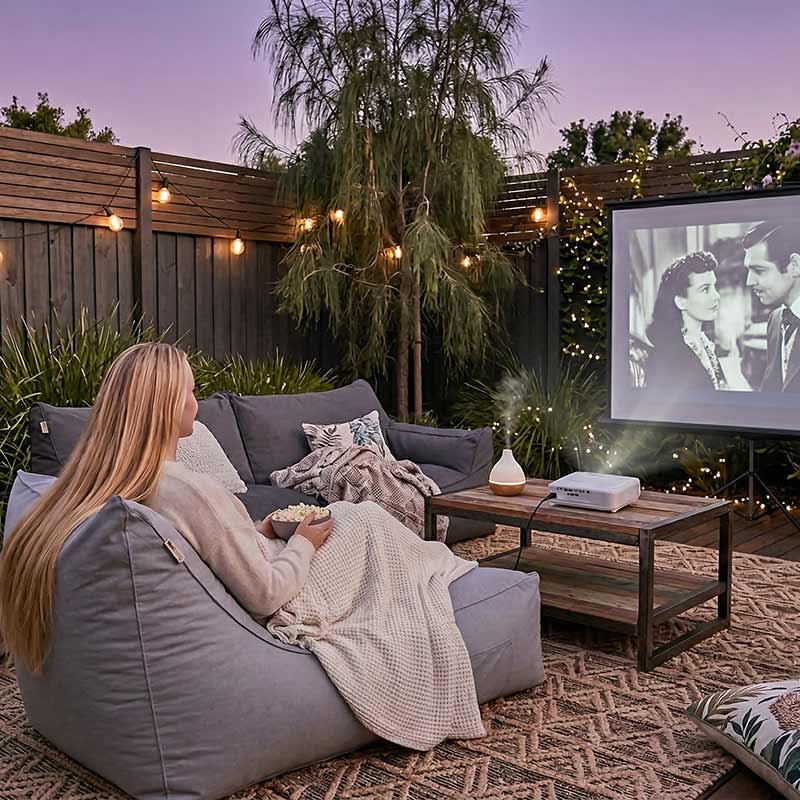 Cinema Bean Bags - Australian backyard outdoor cinema setup with projector screen, fairy lights and blankets, Grey Lachlan Lounger positioned facing the screen, cozy evening atmosphere.