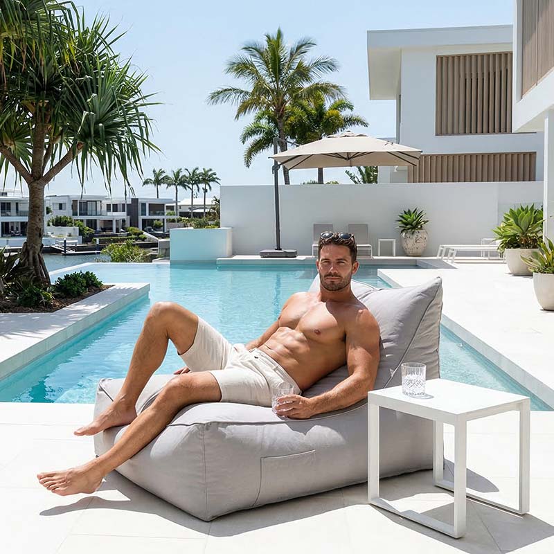 Lifestyle image - Australian resort-style pool area with palm trees, white stone tiles and luxury outdoor setting, Lachlan Bean Bag Lounger  outdoor bean bag by Mooi Living, placed beside the pool.