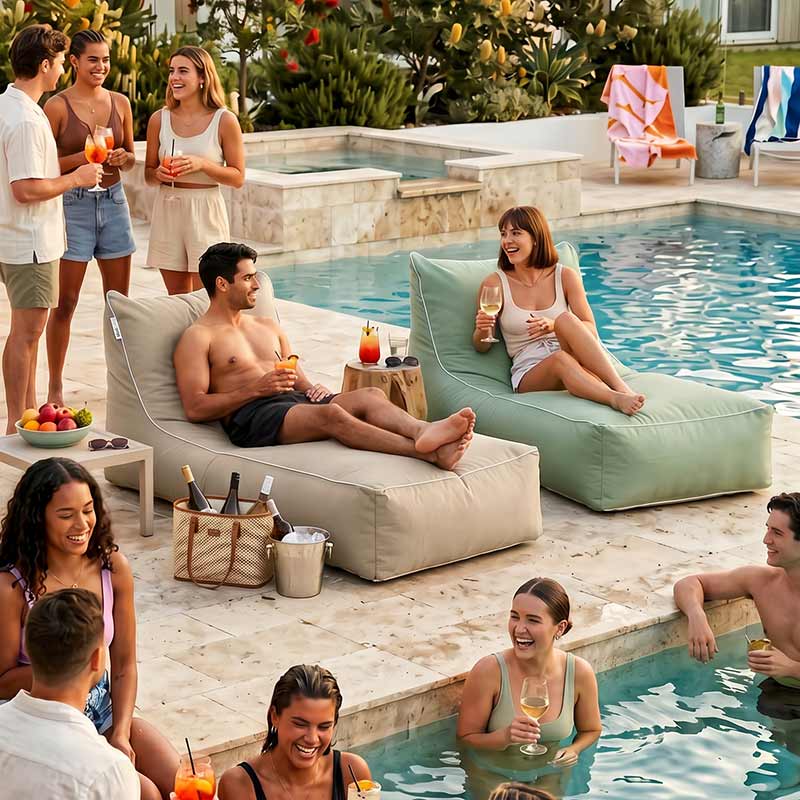 Two people lounging on two Talia Floating outdoor bean bags by Mooi Living, with a group of people enjoying a pool party by a swimming pool.
