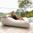 Woman reclining on a Mooi Living Natural Nevaeh double outdoor bean bag sunbed on a timber deck beside a pool, MOSTNEVBB-BEIGE