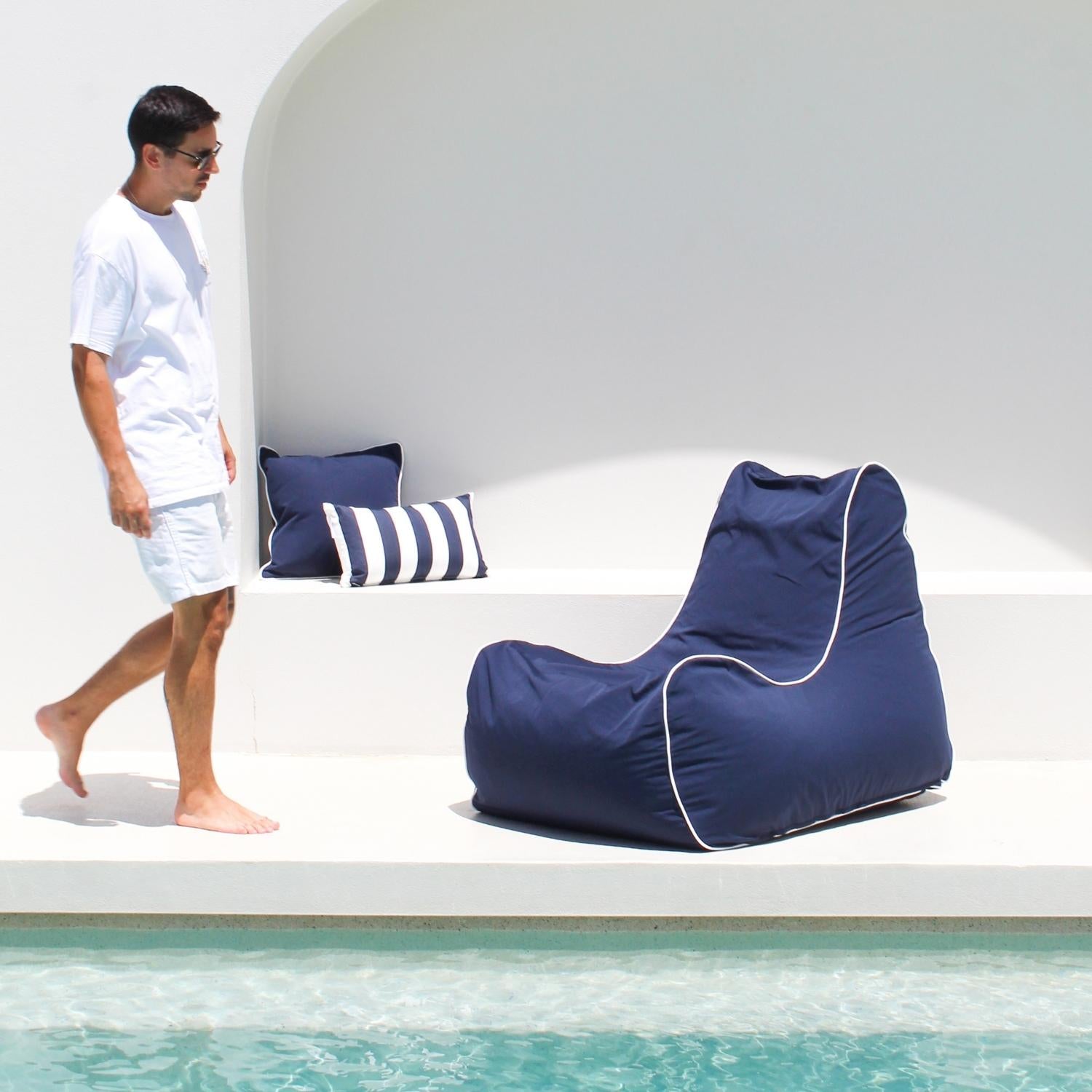 A man walking towards a Navy Bora Bora bean bag Chair with navy and navy white stripes in the background