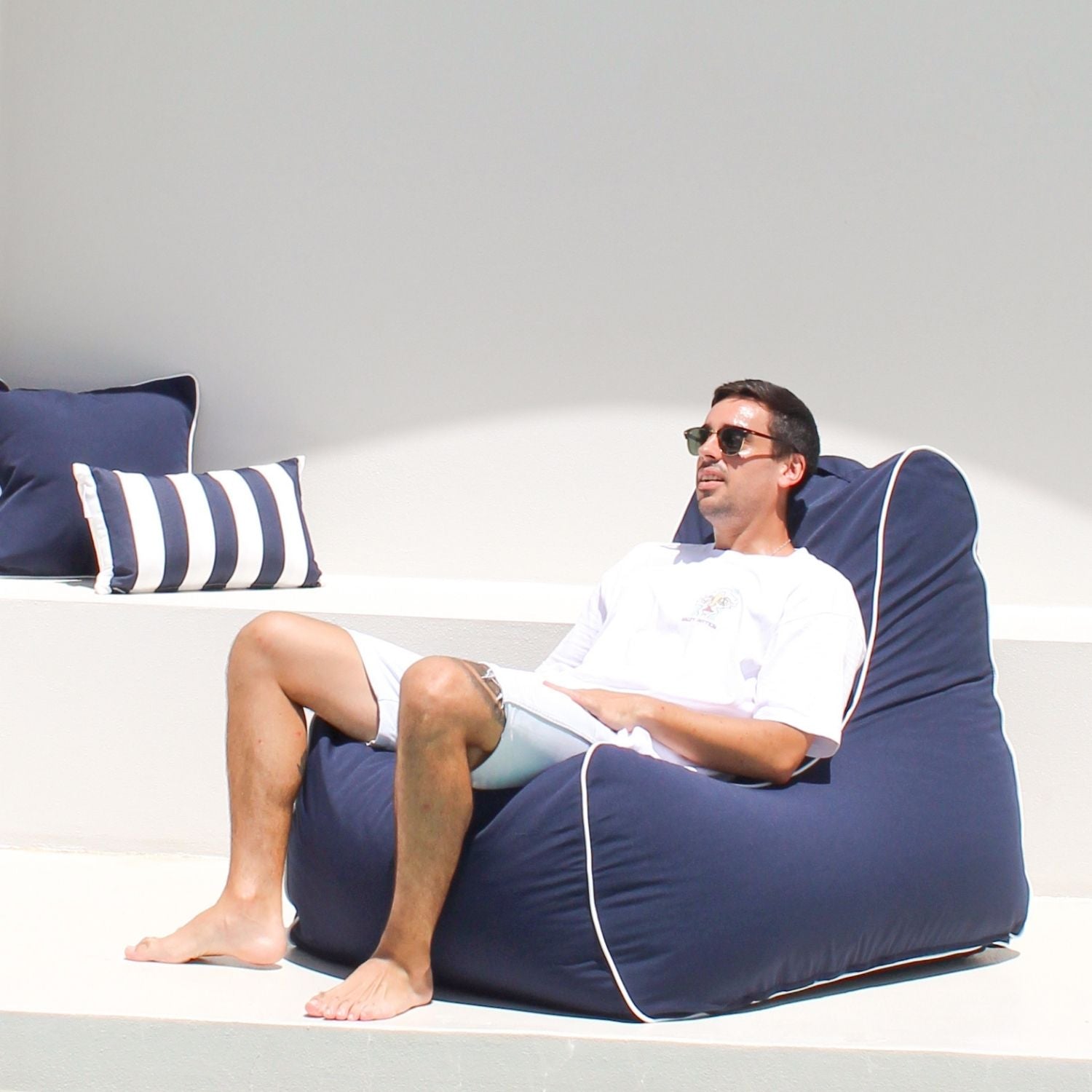 A man sitting and relaxing on a navy Bora Bora bean bag chair with navy and navy whites stripes in the background