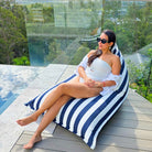 Woman reclining with legs extended on the navy and white striped side of a reversible triangle outdoor bean bag on a timber deck, MOREVSTRIBB-NAVY