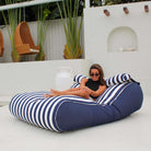 Woman lounging on a Mooi Living Navy Stripe Nevaeh double outdoor bean bag sunbed with navy side panels and white piping, MOSTNEVBB-STRI-NAV