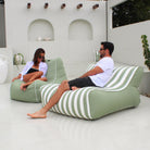 A man and a woman relax on a Bora Bora outdoor bean bag lounge chairs with sage green and white stripes in a modern white patio setting, MOSTRCHILL-BB-GRESTR