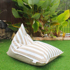 Mooi Living Taupe reversible triangle outdoor bean bag in a tropical garden, showing its taupe and white striped side, MOREVSTRIBB-TPESTR