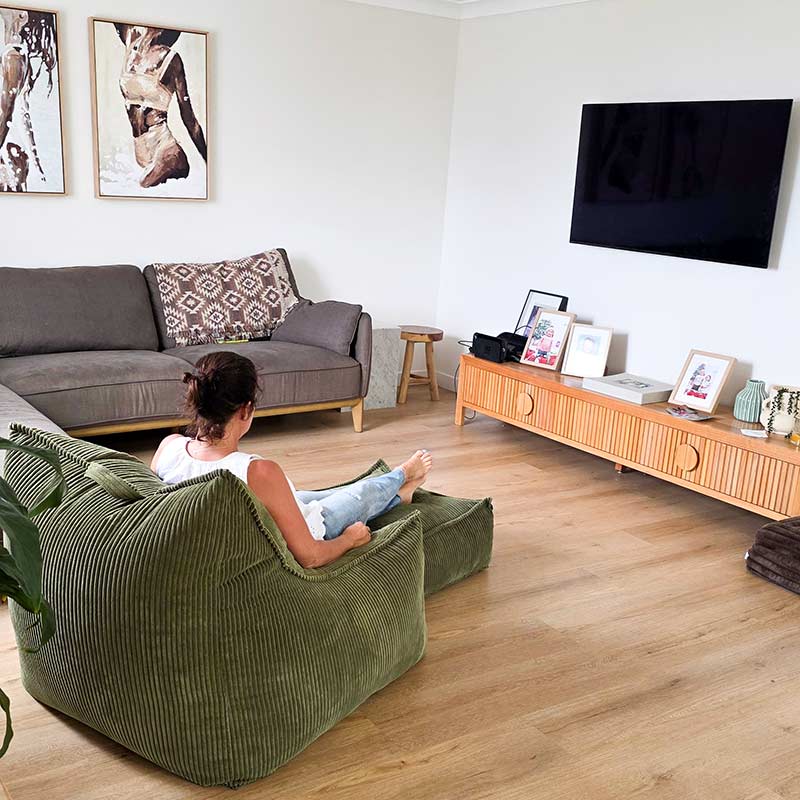 Cord Chair indoor bean bag by Mooi Living in Olive Green in a living room with a woman sitting on the corduroy bean bag chair. This bean bag is perfect for any indoor space.