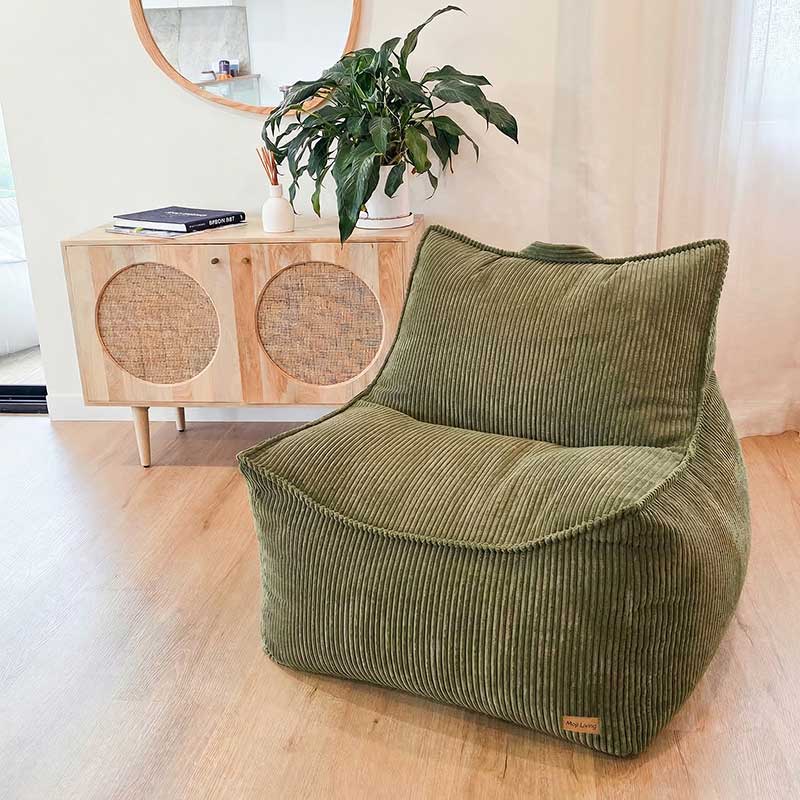 Olive green corduroy bean bag chair in a room with a wooden cabinet and plant.