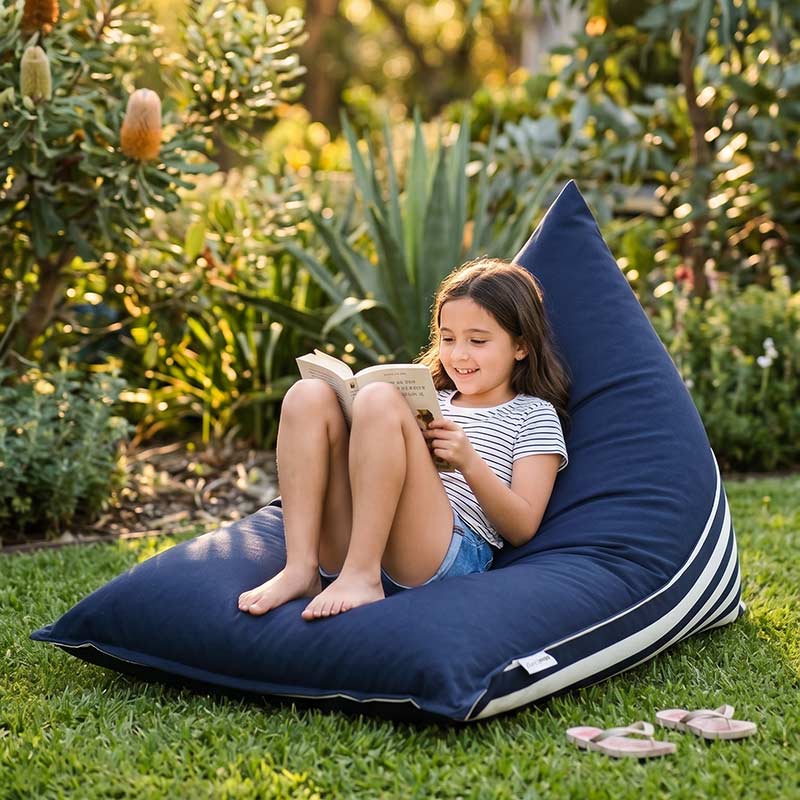 Child reading a book on a Navy Reversible Triangle outdoor bean bag by Mooi Living in a garden.