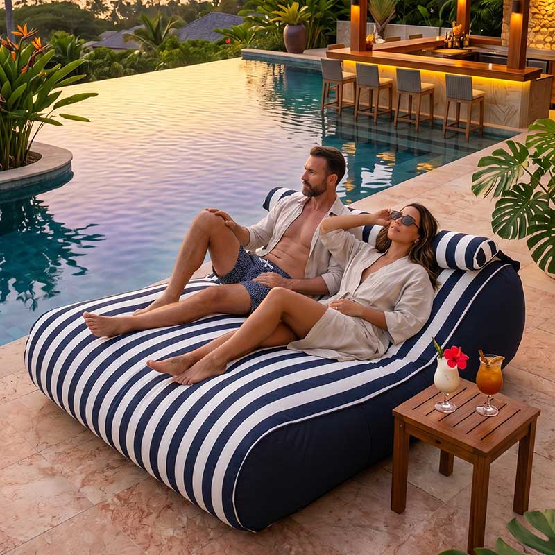 Couple relaxing on a Navy Striped Nevaeh Sunbed outdoor bean bag by Mooi Living by a poolside with drinks and plants.