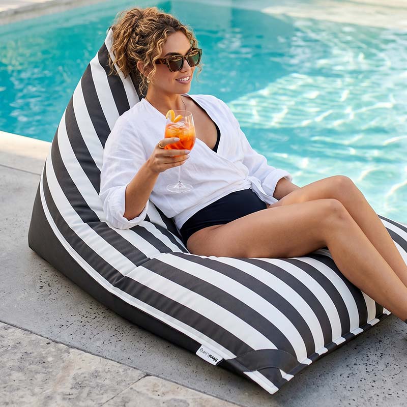 Woman relaxing on an Oyster Black Reversible Triangle outdoor bean bag by Mooi Living with a drink by a pool