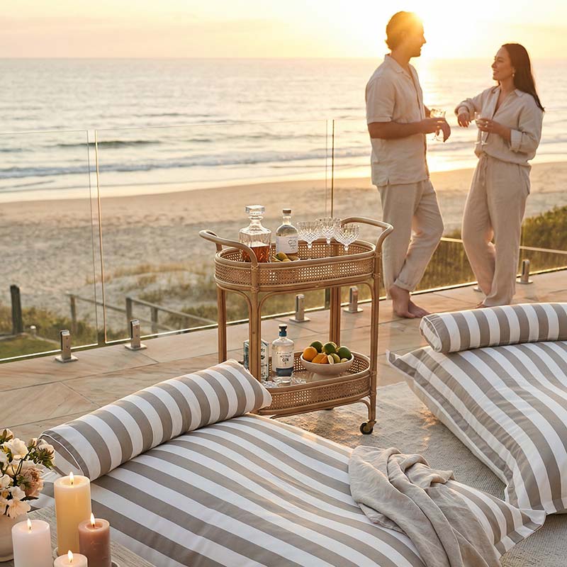 Couple by a bar cart on a deck with Santorini Floating Outdoor Bean Bags by Mooi Living ocean view during sunset