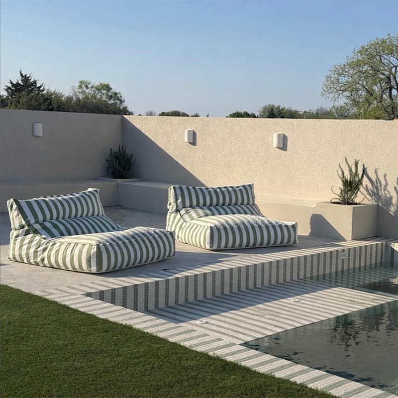 Two striped Lana Lounger outdoor bean bags by Mooi Living by a poolside with a clear sky and greenery.